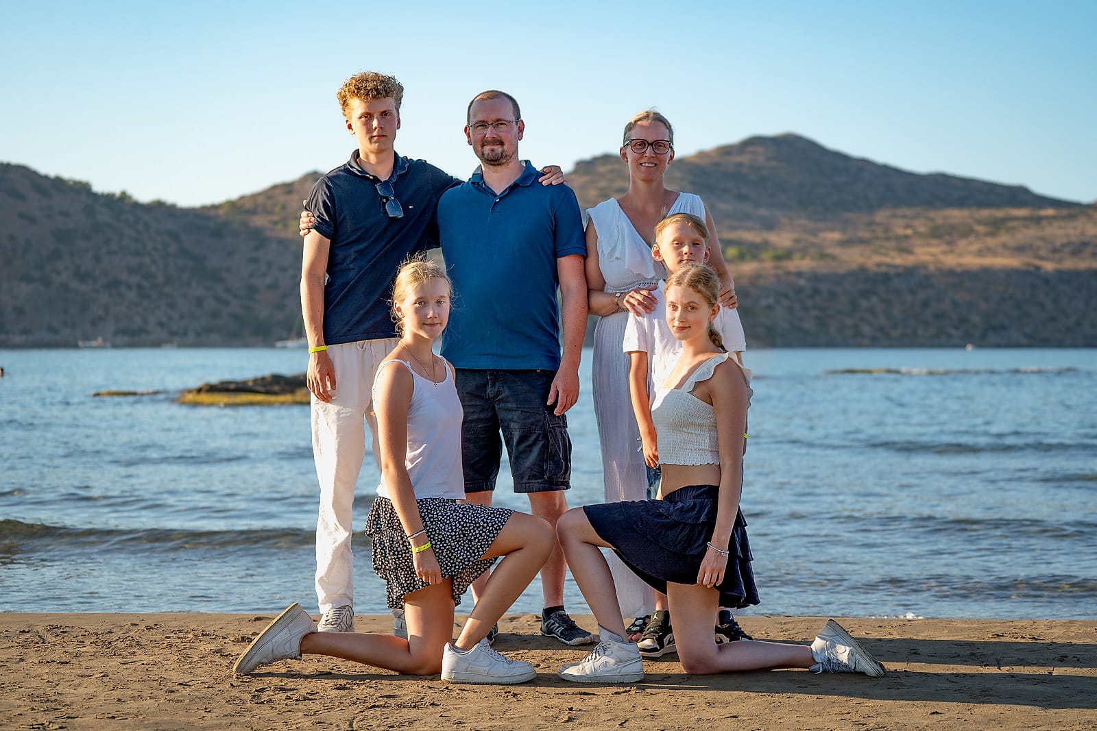 Family of six photographed together on Agia Marina beach with hills behind them