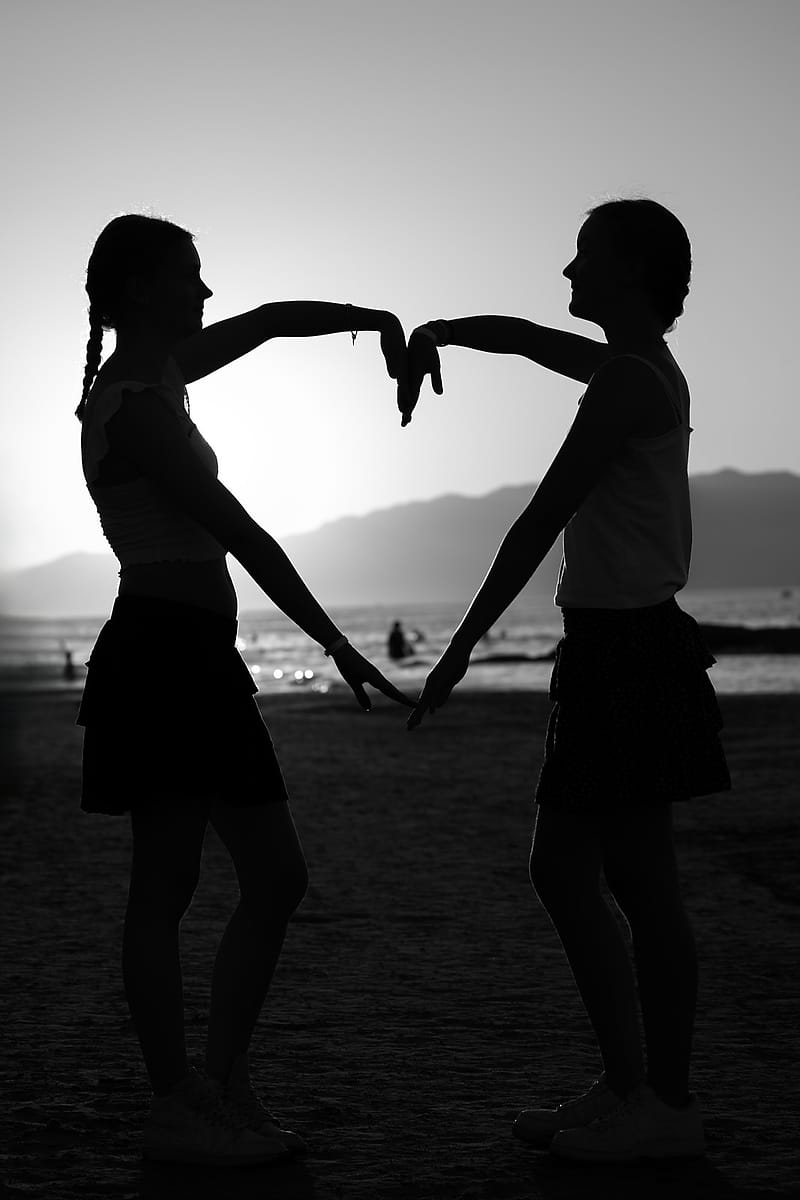 Two sisters forming a heart shape with their hands, silhouetted against the sunset