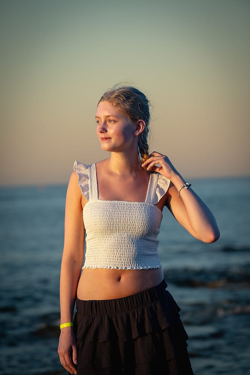 Portrait of a young woman at golden hour with the sea softly blurred behind her
