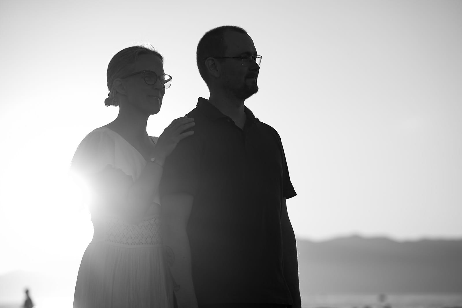 Silhouette of a couple standing together on the beach at sunset, in black and white