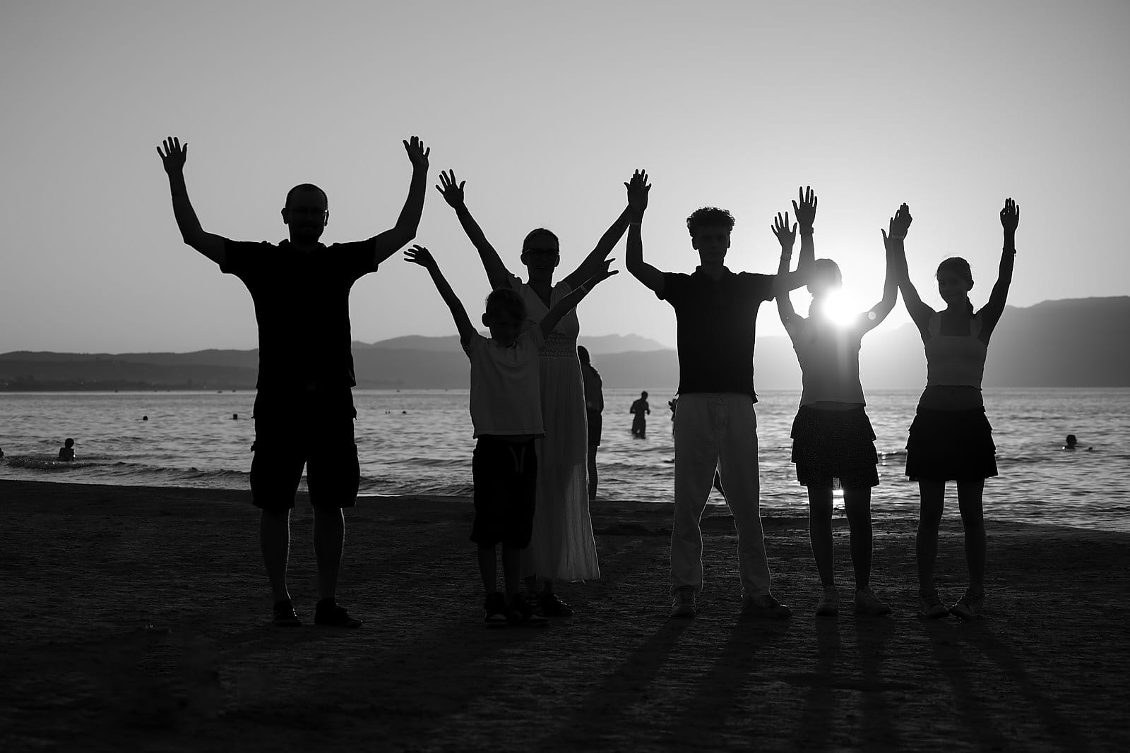 Family silhouette with arms raised on the beach at sunset, in black and white