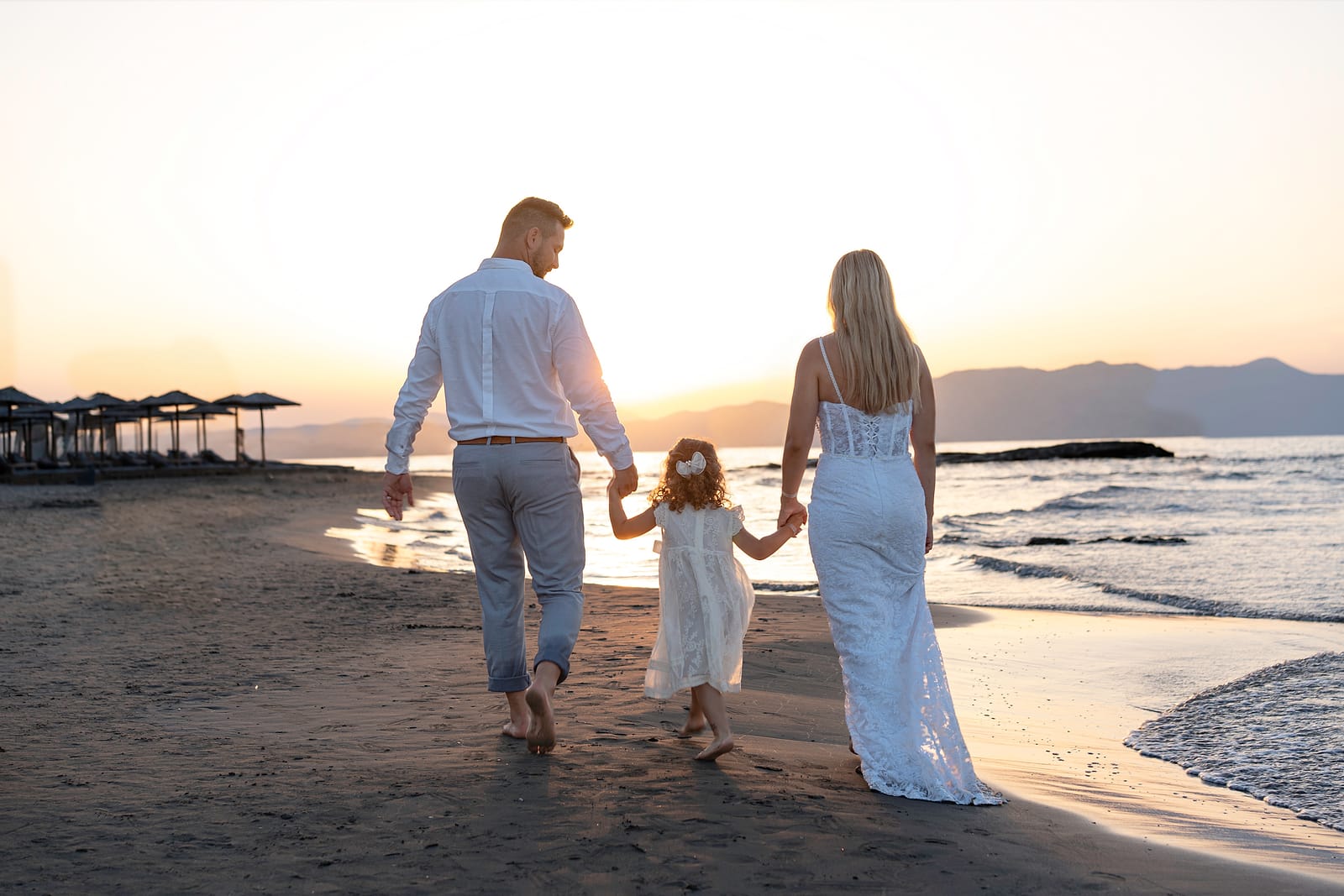 Family walking hand in hand along the shore near Chania at sunset
