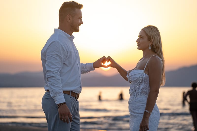 Couple forming a heart with their hands around the setting sun over the sea at Agia Marina