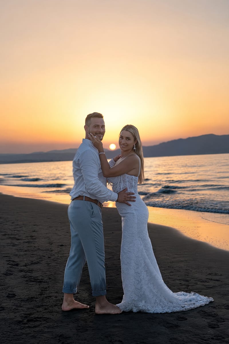 Couple embracing on the beach at sunset, the woman in a long white lace gown